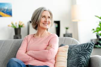 Ältere Frau sitzt lächelnd und selbstbewusst auf dem Sofa